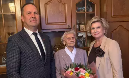 Na zdjęciu widzimy trzy osoby stojące w elegancko urządzonym, domowym wnętrzu, prawdopodobnie podczas uroczystości rodzinnej lub oficjalnej wizyty z okazji jubileuszu.